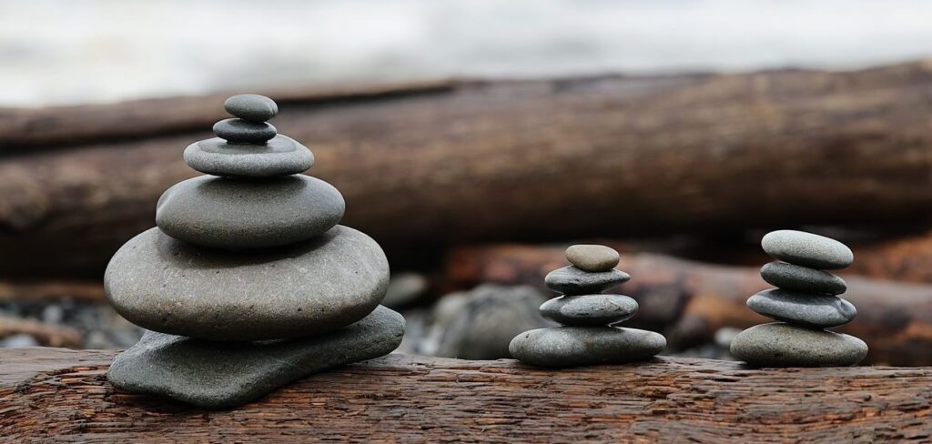 Home Balanced pebble cairns on weathered driftwood at a serene seaside, evoking tranquility and balance.